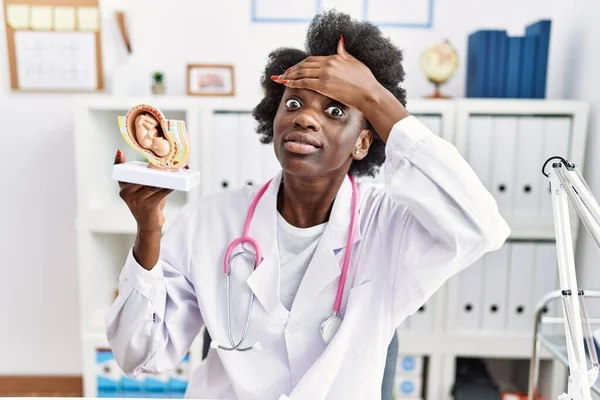 African doctor woman holding anatomical model of female uterus with fetus stressed and frustrated with hand on head, surprised and angry face
