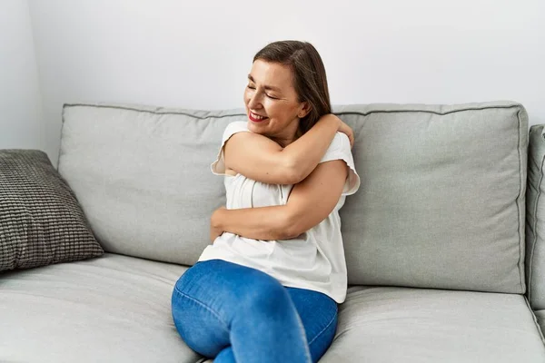 Middle Age Hispanic Woman Smiling Sitting Sofa Hugging Herself Home — Stockfoto