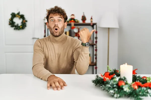 Mladý Pohledný Muž Plnovousem Sedící Stole Vánoční Výzdoby Překvapen Ukazující — Stock fotografie
