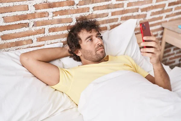 在卧室里用智能手机躺在床上的年轻人 — 图库照片