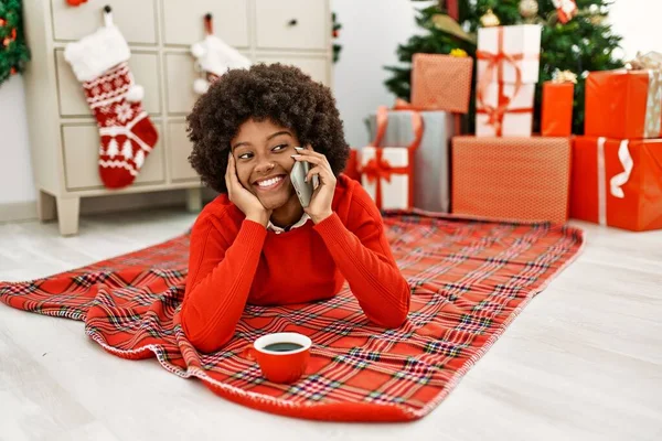 若いアフリカ系アメリカ人女性の話をスマートフォンに横たわっクリスマスツリーによってホーム — ストック写真