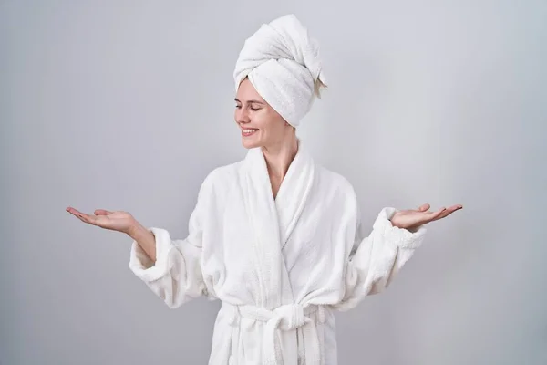 金发女人穿着浴衣笑着 双手张开手掌 展示和宣传比较与平衡 — 图库照片