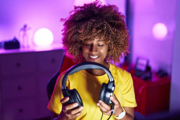 アフリカ系アメリカ人女性ストリーマー笑顔自信を持って保持ヘッドフォンでゲームルーム — ストック写真