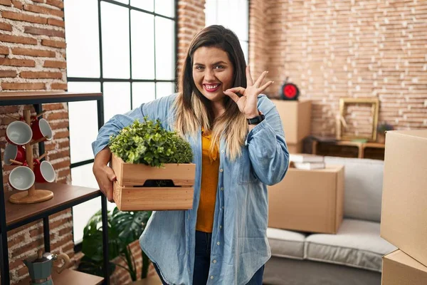 若いヒスパニック系の女性は 指でOkサインを行う新しい家庭所有の植物に移動します 笑顔フレンドリーなジェスチャー優れたシンボル — ストック写真