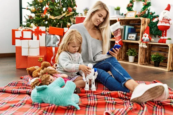 妈妈和女儿在家里玩玩具 用智能手机坐在圣诞树旁 — 图库照片