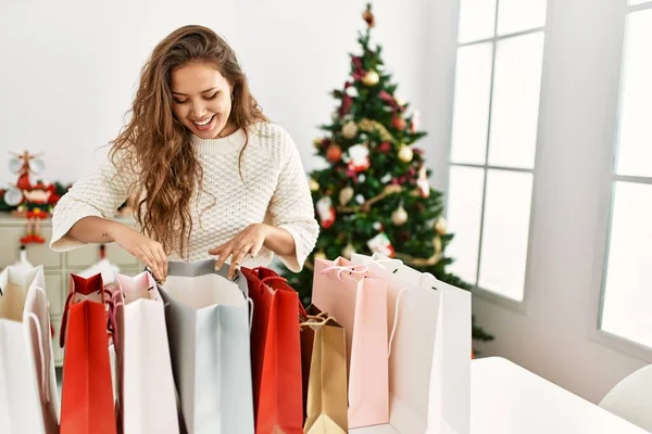 stock image Young beautiful hispanic woman looking shopping bags standing by christmas tree at home