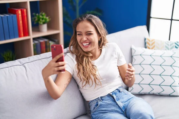 幸せな笑顔で達成を祝うスマートフォンでビデオ通話を行う若いヒスパニック系女性と手を上げと勝者の式 — ストック写真