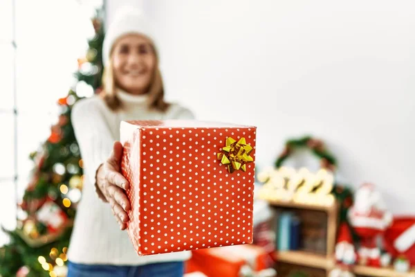 中年妇女笑着自信地拿着礼物站在家里的圣诞树旁 — 图库照片