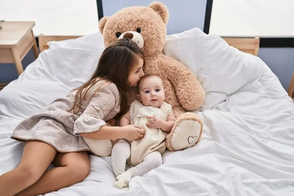 Brother and sister kissing and lying together with teddy bear on bed at bedroom