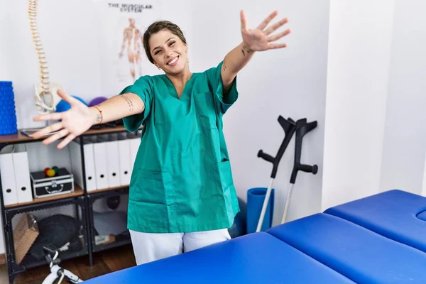 Młoda Latynoska Kobieta Mundurze Fizjoterapeuty Stojąca Klinice Patrząca Kamerę Uśmiechnięta — Zdjęcie stockowe