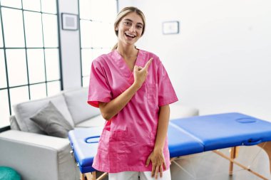 Evde fizyoterapist olarak çalışan genç sarışın kadın yüzünde kocaman bir gülümsemeyle kameraya el ve parmak ile bakıyor.. 