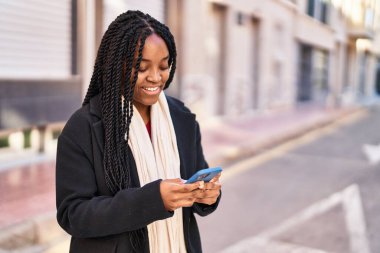 Afro-Amerikalı kadın sokakta akıllı telefon kullanarak kendine güveniyor.
