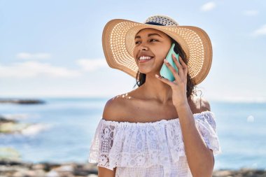 Genç Afrikalı Amerikalı kadın turist, gülümsüyor. Deniz kenarında akıllı telefondan konuşuyor.