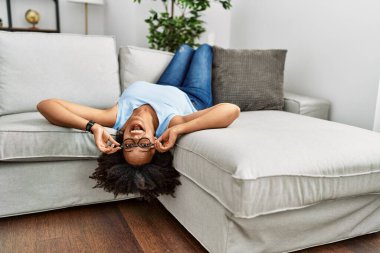 Genç Afro-Amerikan kadın, evinde koltukta kendinden emin bir şekilde yatarken gülümsüyor.