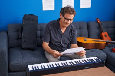 Middle age man musician smiling confident reading music sheet at music studio