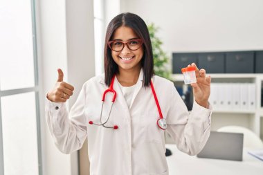 Genç İspanyol doktor elinde mutlu ve pozitif gülümseyen bir kupa tutuyor, başparmağıyla mükemmel ve onay işareti yapıyor. 