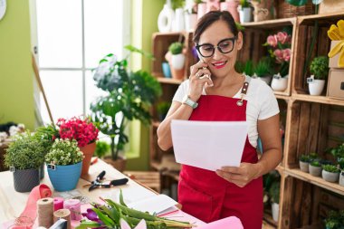 Çiçekçide akıllı telefondan konuşan güzel İspanyol kadın çiçekçi.