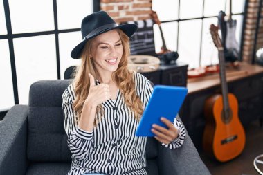 Müzik stüdyosundaki güzel sarışın kadın mutlu ve pozitif gülümseyen tablet kullanıyor, başparmağı mükemmel ve onay işareti yapıyor. 