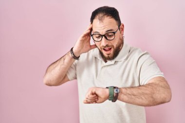 Plus size hispanic man with beard standing over pink background looking at the watch time worried, afraid of getting late 