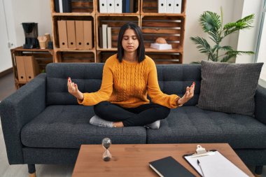 Genç Latin kadın psikoloji hastası klinikte yoga egzersizi yaparken rahatlamış.