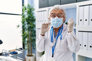 Gri saçlı, doktor üniforması giyen ve elinde şırıngayla gururla bağıran, zaferi ve başarıyı kutlayan yaşlı bir kadın. 