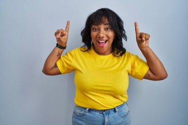 Mavi arka planda duran İspanyol kadın şaşırmış, şaşırmış ve parmaklarıyla işaret ediyor ve kollarını kaldırıyordu.. 