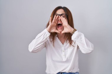 Esmer kadın izole edilmiş beyaz arka planda duruyor ve elleri ağzında kızgın bir şekilde bağırıyor. 