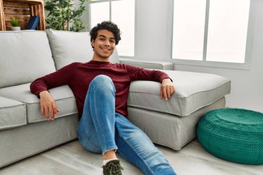 Genç İspanyol adam gülümsüyor. Mutlu bir şekilde evde yerde oturuyor..