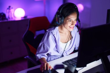 Young beautiful hispanic woman streamer playing video game using computer at gaming room