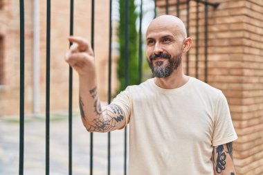 Genç kel adam gülümsüyor. Kendine güveni tam, parmağıyla sokağı gösteriyor.