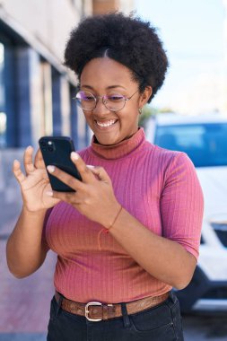 Afro-Amerikalı kadın sokakta akıllı telefon kullanarak kendine güveniyor.