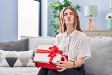 Elinde hediyeyle kameraya bakan güzel bir kadın öpüşmeyi üflüyor. Sevimli ve seksi. aşk ifadesi. 