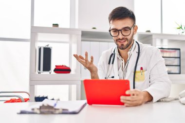 Genç İspanyol doktor dokunmatik ped kullanıyor. Klinikten video çağrısı alıyor.