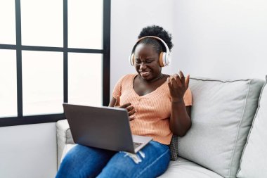Young african american woman listening to music sitting on sofa at home