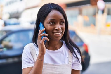 Genç Afrikalı Amerikalı kadın gülümsüyor. Kendine güveni tam. Sokakta akıllı telefondan konuşuyor.