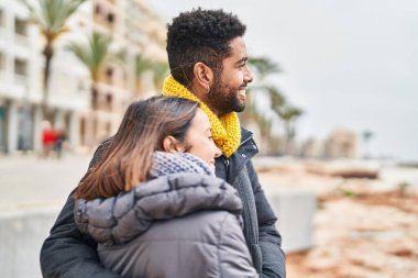 Kadın ve erkek gülümsüyor. Kendilerine güveniyorlar. Deniz kenarında sarılıyorlar.