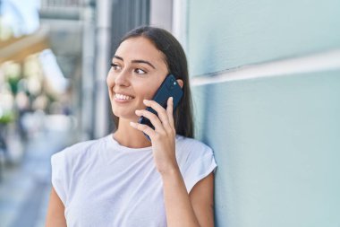 Genç, güzel, İspanyol bir kadın gülümsüyor ve caddede akıllı telefondan konuşuyor.