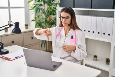 Beautiful doctor woman working on online appointment with angry face, negative sign showing dislike with thumbs down, rejection concept 