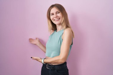 Pembe arka planda duran sarışın beyaz kadın gülümseyerek doğal bir şekilde içeri girmeye davet ediyor. 