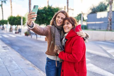 Two women mother and daughter make selfie by smartphone at street