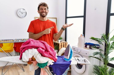 Çamaşır odasında giysilerini ütüleyen genç İspanyol adam kameraya hayret ediyor ve gülümsüyor.. 