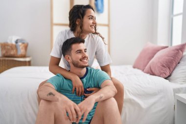 Young hispanic couple hugging each other sitting on bed at bedroom