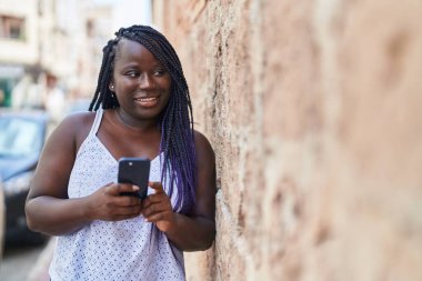 Afro-Amerikalı kadın sokakta akıllı telefon kullanarak kendine güveniyor.