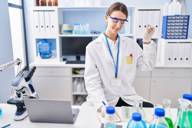 Young caucasian woman scientist writing report holding sample at laboratory