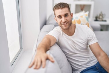 Evdeki koltukta kendinden emin gülümseyen beyaz bir genç.