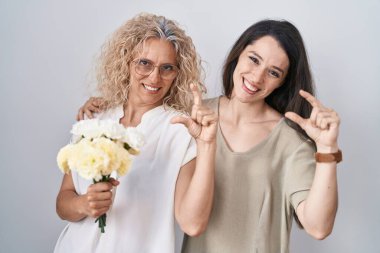 Anne ve kızı ellerinde bir buket beyaz çiçek tutuyorlar gülümsüyorlar ve el hareketleriyle hareket ediyorlar parmaklarıyla işaret veriyorlar ve kameraya bakıyorlar. ölçüm kavramı. 