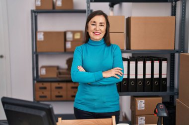 Middle age woman ecommerce business worker standing with arms crossed gesture at office