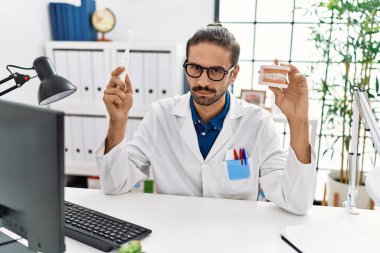 Young hispanic dentist man holding denture and toothbrush skeptic and nervous, frowning upset because of problem. negative person. 