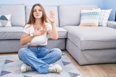 Beyaz bir kadın, oturma odasında yerde oturmuş, avucunda ve göğsünde el pençe ile yemin ediyor, sadakat yemini ediyor. 