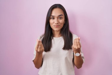 Pembe arka planda duran genç İspanyol kadın elleriyle para hareketi yapıyor, maaş istiyor, milyonerlik işi yapıyor. 